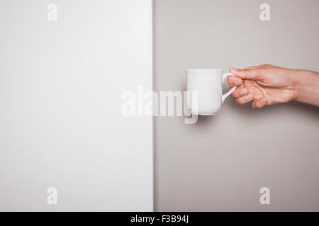 Une main tient une tasse blanc contre un fond blanc et vert Banque D'Images