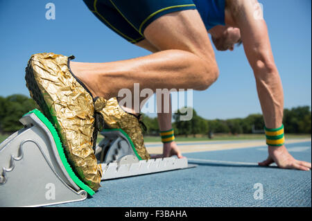 Dans l'or de l'athlète à partir de chaussures de course les blocs de départ sur une piste de course bleu Banque D'Images