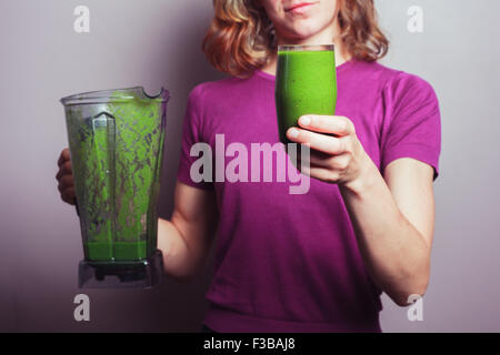 Une jeune femme en pourpre est titulaire d'un mélangeur et un verre avec smoothie aux fruits vert Banque D'Images