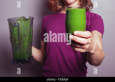 Une jeune femme en pourpre est titulaire d'un mélangeur et un verre avec smoothie aux fruits vert Banque D'Images