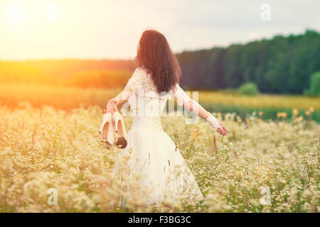 Young bride holding shoes walking on the flower meadow Banque D'Images