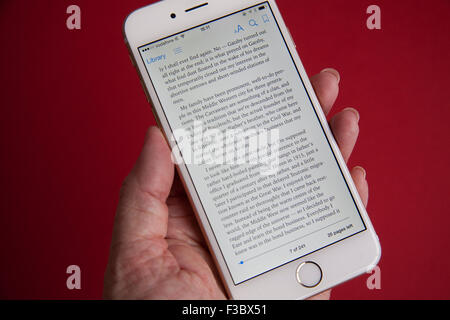 La lecture d'un ebook sur un or et blanc Apple iPhone 6 sur un fond rouge Banque D'Images