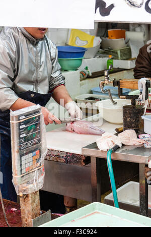 L'homme, visage caché par un panneau, la coupe et l'éviscération fugu, le poisson-globe Blanc en haut travail sur la partie cuisine de poissons en magasin marché Kuromon Ichiba, Osaka. Banque D'Images