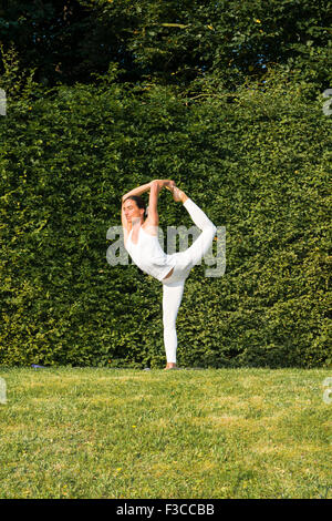 Jeune femme, portant un costume blanc, est la pratique de l'hatha-yoga piscine entre les arbres, montrant la pose : natarajasana, seigneur shi Banque D'Images