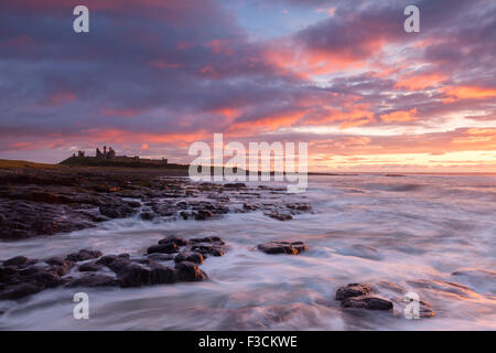 Château de Dunstanburgh lever du soleil, vagues se brisant sur le rivage rocheux le long de Craster, Northumberland, Angleterre Banque D'Images