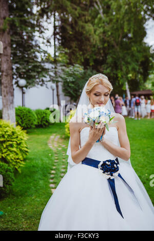 Mariée en robe blanche en été parc verdoyant avec un bouquet dans la main Banque D'Images