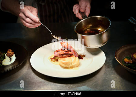 Restaurant chef pouring sauce sur le plat de porc Banque D'Images