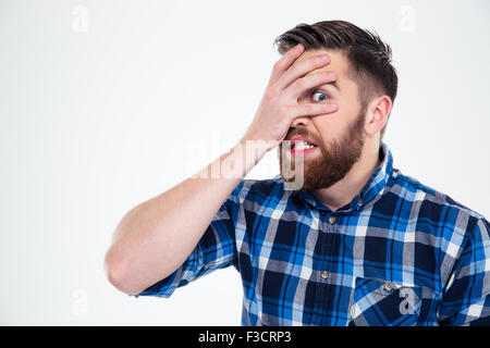 Portrait d'un homme effrayé couvrant son visage avec palm et à la caméra à l'intermédiaire de doigts isolé sur fond blanc Banque D'Images