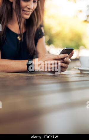Portrait of young woman using smart phone dans un café en plein air. Femme lisant un message texte sur son téléphone mobile. Banque D'Images