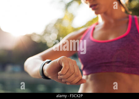 Jeune femme à sa remise en forme au smart watch tout en prenant une pause dans l'entraînement sportif. Contrôle de la sportive remise en forme d'impulsions sur Banque D'Images