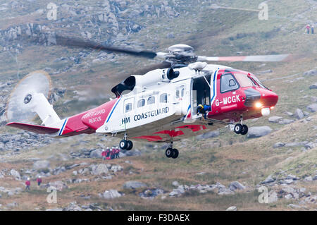 Bristow habilement d'hélicoptères de sauvetage à l'approche d'un terrain accidenté de l'atterrissage, ainsi que d'une équipe de sauvetage en montagne de descendre dans l'arrière-plan Banque D'Images