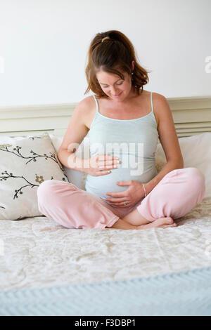 Smiling pregnant woman sitting on bed Banque D'Images