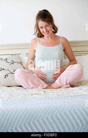 Smiling pregnant woman sitting on bed Banque D'Images