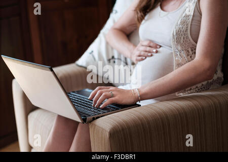 La mi-section of pregnant woman using laptop Banque D'Images
