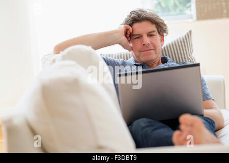 Mature man using laptop on sofa Banque D'Images