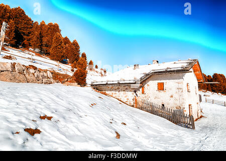 Chalet alpin entouré par une clôture dans la neige entre les sommets enneigés et les forêts de pins sur une journée ensoleillée en hiver Banque D'Images