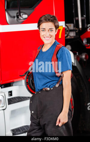 Heureux pompier femelle debout contre les pompiers Banque D'Images