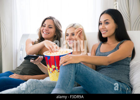 Portrait de trois professionnels girlfriends eating popcorn et regarder la télé à la maison Banque D'Images