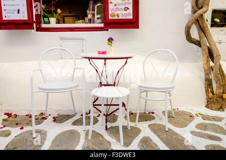 Dans un café sur l'île grecque de Chora Mykonos, Grèce dans une allée pavée pavée traditionnelle avec volets de fenêtre rouge, chaises, t Banque D'Images