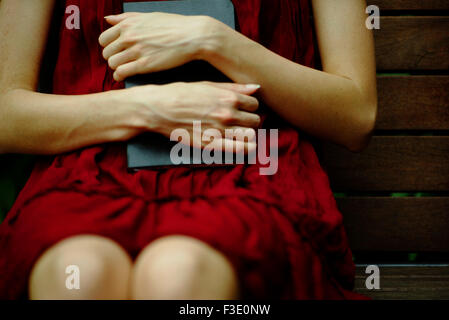 Femme assis sur un banc, tenant de façon protectrice contre poitrine journal Banque D'Images
