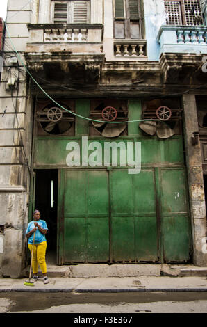 Femme avec un balai se trouve en face d'une porte massive avec trois fans géant d'une ancienne usine à La Havane, République de Cuba Banque D'Images