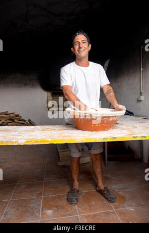 Young baker mixer la pâte dans un bol à la main pour être cuit dans un four traditionnel en briques Banque D'Images