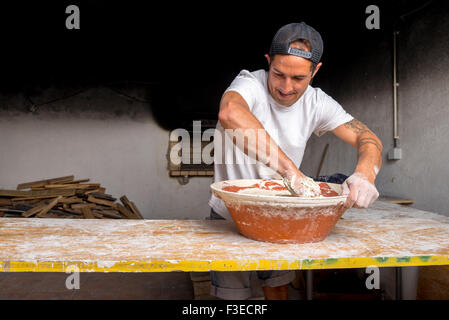 Young baker mixer la pâte dans un bol à la main pour être cuit dans un four traditionnel en briques Banque D'Images