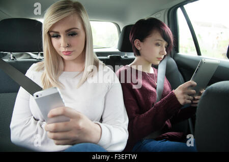 Deux sœurs adolescentes dans le siège arrière d'une voiture tenant une tablette ipad et téléphone mobile. Banque D'Images