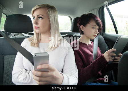 Deux sœurs adolescentes dans le siège arrière d'une voiture et d'un holding tablet ipad et téléphone mobile. Banque D'Images