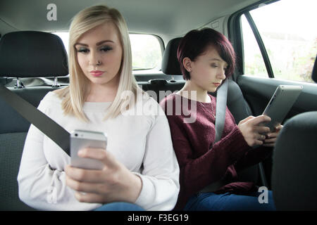 Deux sœurs adolescentes dans le siège arrière d'une voiture et d'un holding tablet ipad et téléphone mobile. Banque D'Images