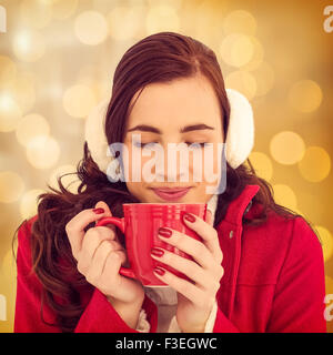 Image composite de femme dans des vêtements d'hiver bénéficiant d'une boisson chaude les yeux fermés Banque D'Images