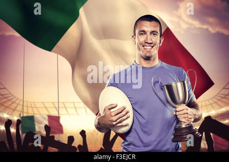 Image composite de portrait of smiling rugby player holding trophy et ball Banque D'Images