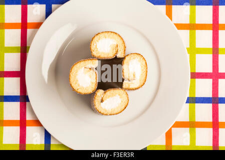 Quatre biscuits roulés et farcis de crème sur une nappe à rayures colorées Banque D'Images