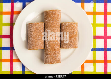 Quatre biscuits roulés et farcis de crème sur une nappe à rayures colorées Banque D'Images