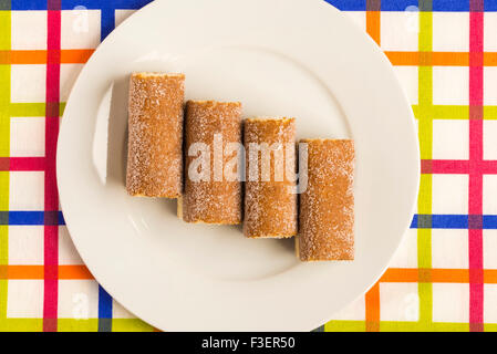 Quatre biscuits roulés et farcis de crème sur une nappe à rayures colorées Banque D'Images