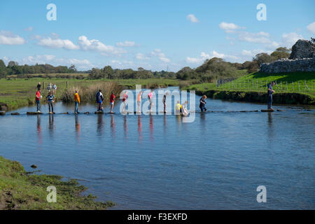 Les enfants en utilisant des pierres de gué pour traverser la rivière près de Ogmore Castle Ogmore, South Glamorgan, Pays de Galles, Royaume-Uni Banque D'Images