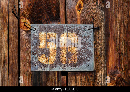 Old rusty plaque avec numéro de maison cloué jusqu'à un mur en bois d'une grange Banque D'Images