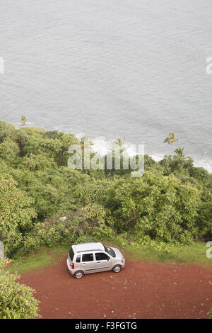 Voiture garée sur la masse de sol rouge entourée de verdure et de mer ; Goa Inde ; Banque D'Images