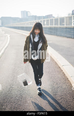 Jeune belle asiatique brune cheveux long hipster femme marche dans la ville, à sourire à la baisse pendant le coucher du soleil en rétro-éclairage - le bonheur, le plaisir, insouciance concept Banque D'Images