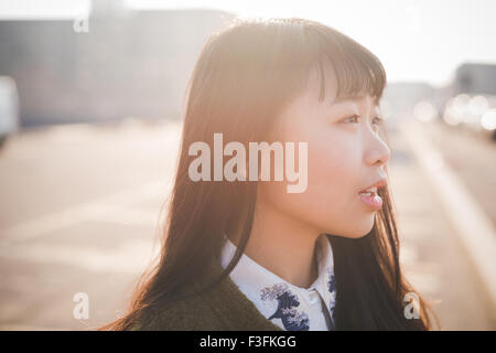 Portrait of young belle asiatique brune cheveux long hipster femme dans la ville, donnant sur la gauche, pensive, dans la ville au cours de Banque D'Images