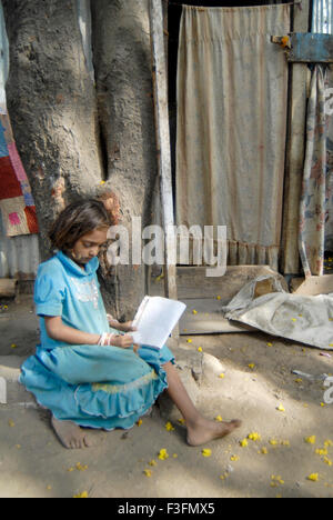 Une fille de l'ouvrier routier apprend Marathi alphabets sous un arbre ; Bombay maintenant Mumbai Maharashtra ; Inde ; Banque D'Images