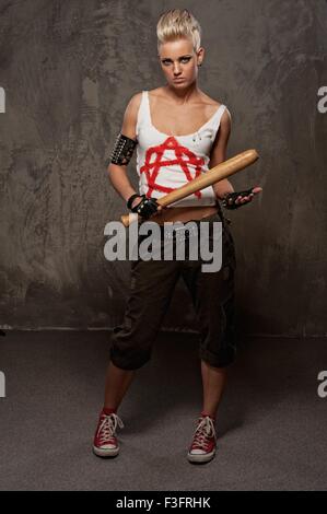 Punk girl avec un bâton de baseball à l'arrière-plan gris. Banque D'Images