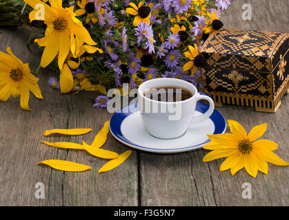 Tasse de café, cercueil, fleurs, pétales et fleurs sauvages sur une vieille table, une nature morte, une carte de fête, une carte de vœux, un sujet Banque D'Images
