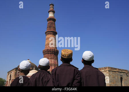 Les enfants faisant la prière religieuse Namaz en face de Qutab Minar tour de grès rouge de l'art musulman Indo Delhi Banque D'Images