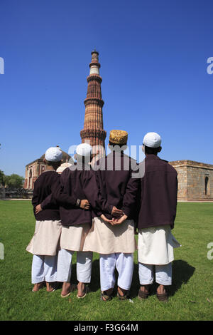 Les enfants faisant la prière religieuse Namaz en face de Qutab Minar tour de grès rouge ; l'art musulman Indo Delhi Banque D'Images