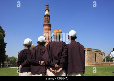 Les enfants faisant la prière religieuse Namaz en face de Qutab Minar tour de grès rouge de l'art musulman Indo Delhi Banque D'Images