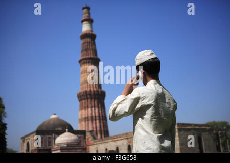 Garçon musulman talking on mobile phone at Qutab Minar construit en 1311 en grès rouge l'art musulman Indo tour Delhi Banque D'Images