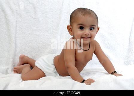 Bébé en couches culottes et amulette autour du cou et des mains allongé sur fond blanc M.# 152 Banque D'Images