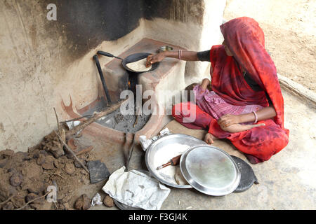 Une femme faisant du pain de blé ou rotis sur une cheminée en prenant dans l'enfant ; au tour du Rajasthan en Inde ; Banque D'Images