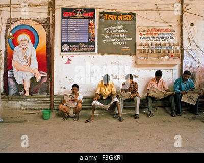 Les gens qui lisent les quotidiens assis sur des tuyaux d'eau ; Bombay ; Mumbai ; Maharashtra ; Inde ; Asie Banque D'Images